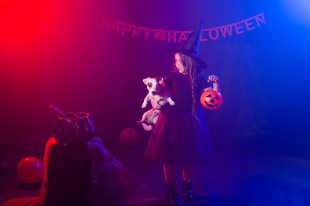 Garota engraçada criança fantasiada de bruxa para o Halloween com a abóbora Jack e o cachorro.