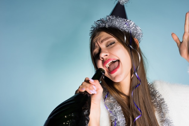 Garota engraçada e bêbada celebra o ano novo, canta em uma garrafa de champanhe