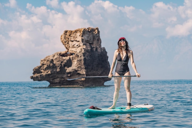 Garota engraçada em um maiô com um remo nada em uma prancha de SUP no mar Estilo de vida saudável e conceito de recreação