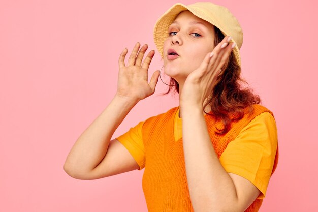 Garota engraçada em um suéter laranja em chapéu amarelo gesto com a mão fundo rosa inalterado