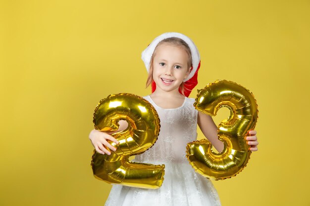 Garota engraçada feliz com chapéu vermelho de Papai Noel de Natal com números de balão em fundo amarelo