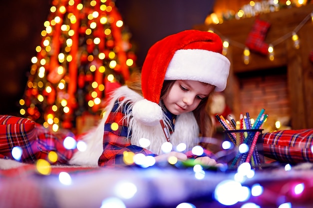 Garota engraçada no chapéu de Papai Noel escreve carta para o Papai Noel