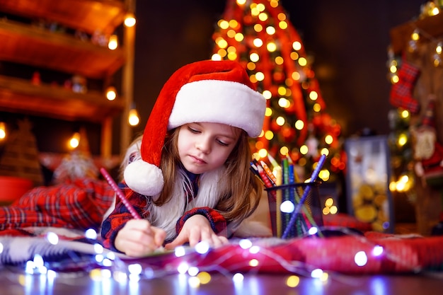 Garota engraçada no chapéu de Papai Noel escreve carta para o Papai Noel