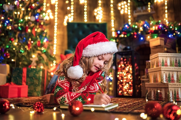 Garota engraçada no chapéu de Papai Noel escreve carta para o Papai Noel