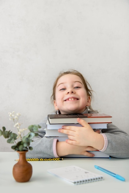 Garota engraçada sentada à mesa abraçando entusiasticamente uma pilha de livros amor pela leitura