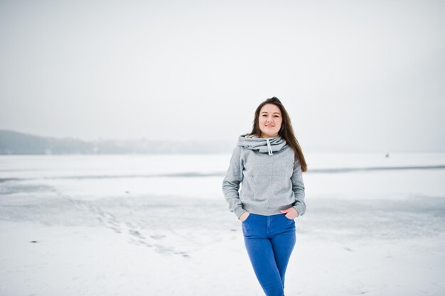 Garota engraçada usa suéter com capuz e jeans no lago congelado no dia de inverno