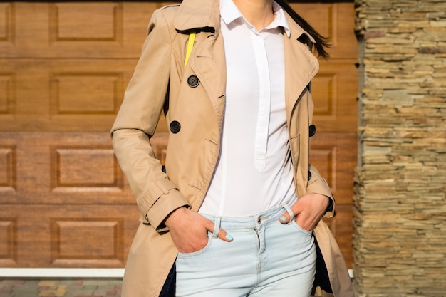 Garota esbelta em um casaco bege, jeans azul e camisa branca ao ar livre