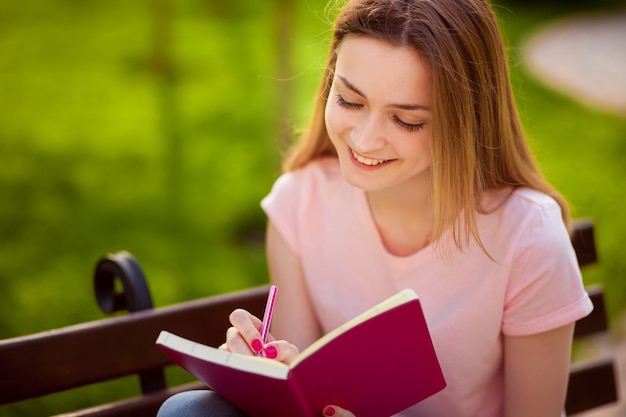 Garota escrevendo em um caderno, sentada em um banco no parque