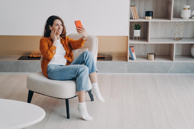 Garota espanhola feliz tendo chamada de vídeo em casa e conectando fones de ouvido