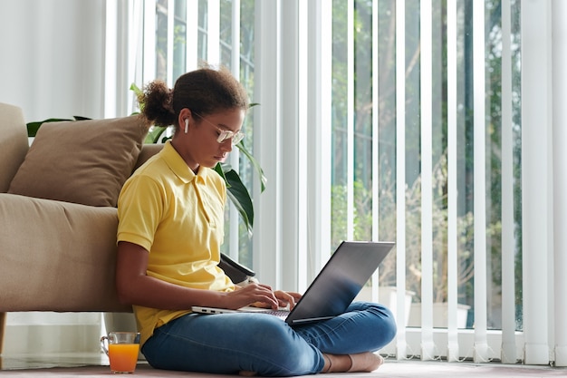Garota esperta em vidro trabalhando em um laptop na sala de estar, ela se esquivando de sua cidade natal para a aula de ciência da computação