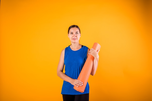 Garota esportiva com um tapete de fitness em uma parede laranja