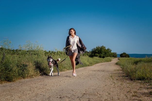 Garota esportiva correndo com um cachorro, o husky siberiano, na estrada