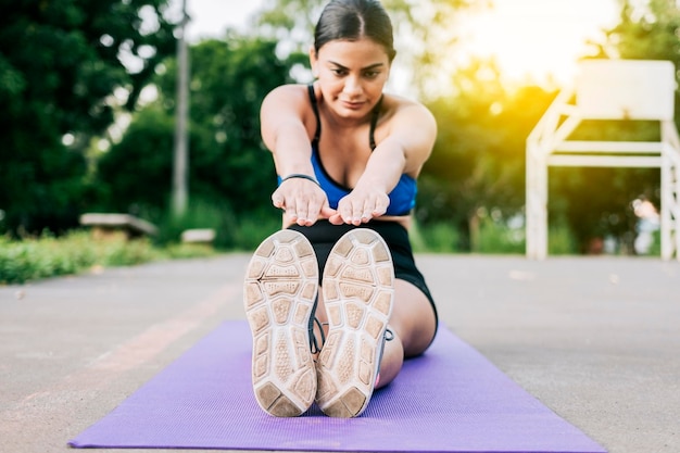 Garota esportiva esticando as pernas sentada em uma esteira em um parque Atleta mulher sentada fazendo alongamento de perna em um parque Atleta sentada em uma esteira esticando as pernas em um parque