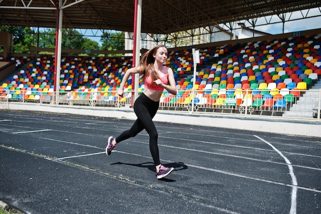 Garota esportiva fitness em roupas esportivas no estádio esportes ao ar livre mulher sexy feliz correndo na esteira atlética no estádio