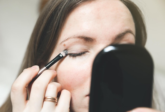 Garota está aplicando sombra de maquiagem com um pincel Conceito de foto de beleza