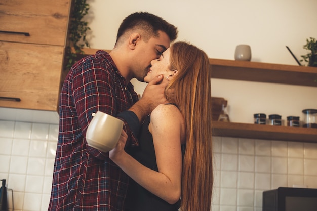 garota está segurando uma xícara enquanto é beijada pelo amante