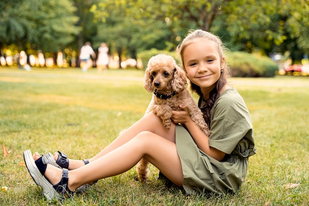 Garota está sentada em um gramado verde com um cachorro poodle.