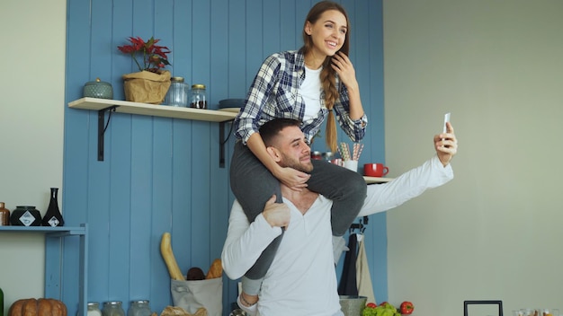 Garota está sentada no pescoço do namorado enquanto ele tira retrato selfie na câmera do smartphone