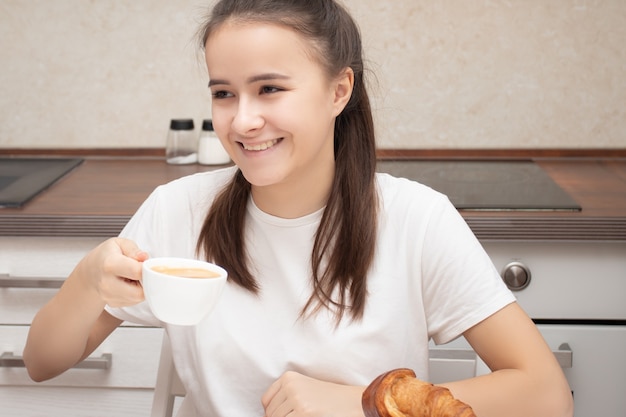 Garota européia de manhã em casa tomando café com croissants