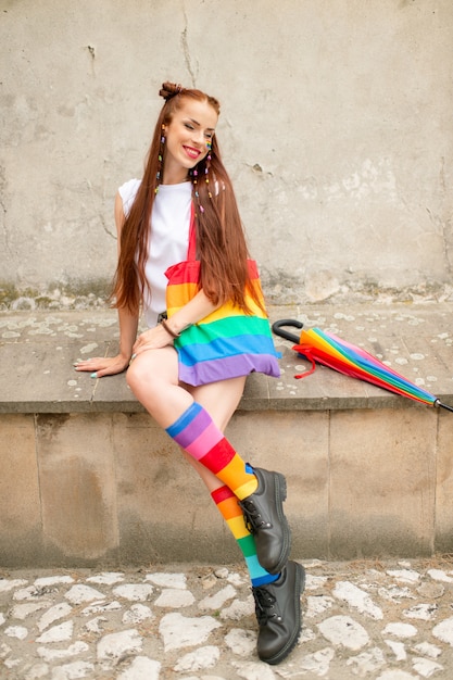 Garota fashion em meias coloridas usando botas masculinas. lésbica elegante com arco-íris lgbt no rosto posando ao ar livre