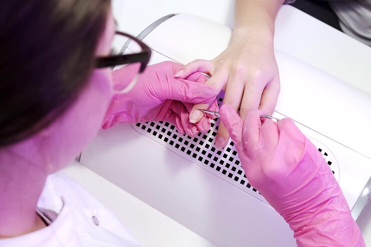 Foto garota faz manicure em um salão de beleza cuidados com as unhas manicure em luvas cor de rosa corta as cutículas no dedo com uma pequena tesoura closeup procedimentos cosméticos