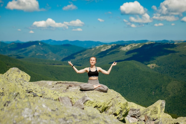 Garota fazendo exercício de ioga pose de lótus no topo da montanha