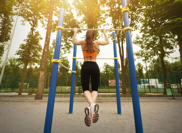 Garota fazendo flexões de treino em bar em quadra de esportes no parque, vista traseira