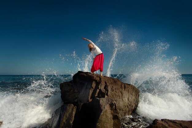 Garota fazendo ioga na colina. Oceano em ondas