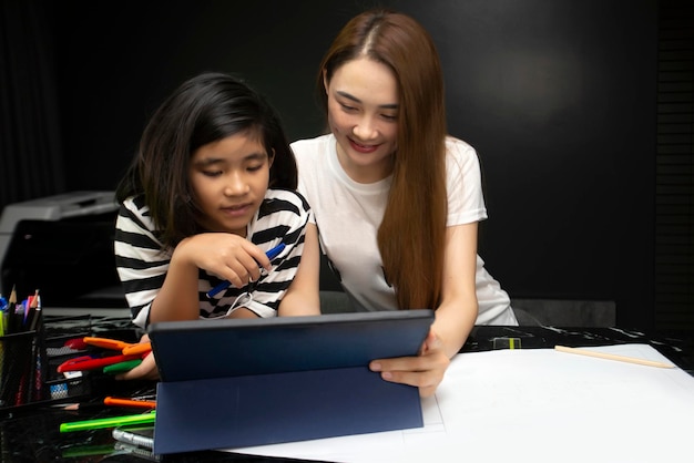 Garota fazendo lição de casa com a mãe na educação on-line da tela do tablet à noite