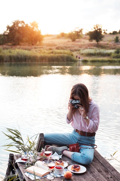 Garota fazendo piquenique em um píer de madeira na margem de um rio brilhante de verão