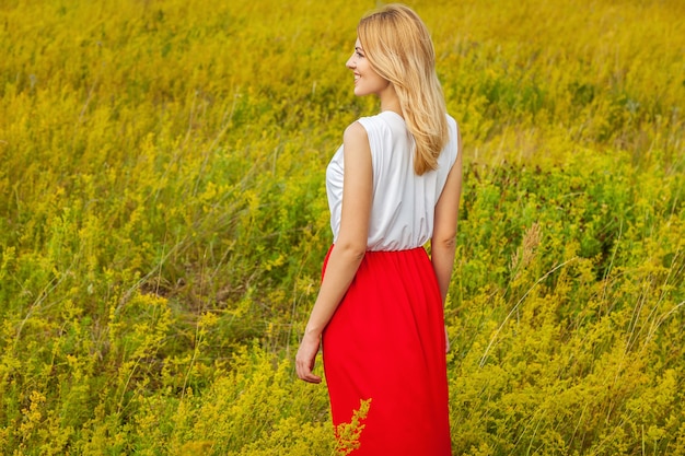 Garota fazendo selfie. loira linda em um vestido vermelho-branco faz selfie no campo em seu telefone.