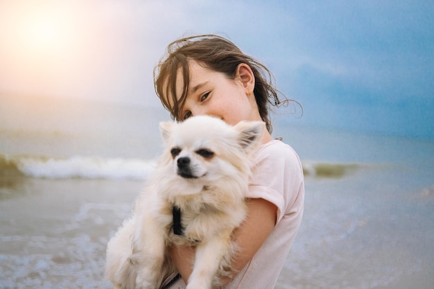 Garota feliz abraçando seu cachorrinho chihuahua à beira-mar contra o céu azul fecha os melhores amigos