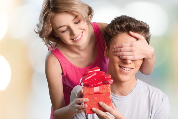 Garota feliz cobrindo os olhos do namorado com as mãos e dando um presente