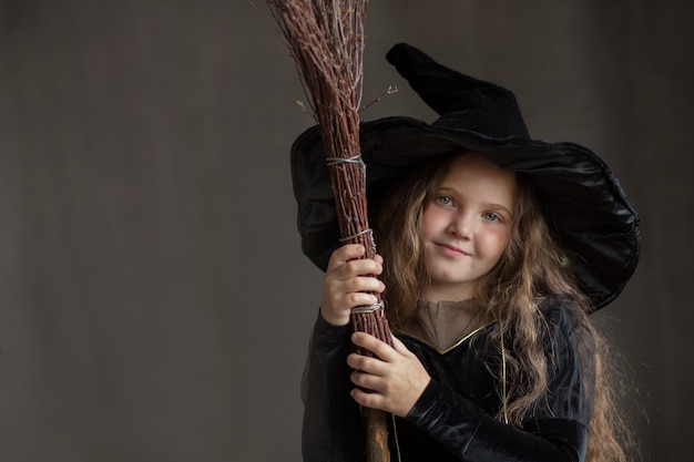 Garota feliz com fantasia de bruxa de halloween em fundo cinza