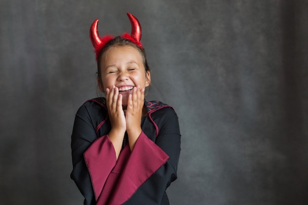 Garota feliz com maldita fantasia de halloween na parede cinza