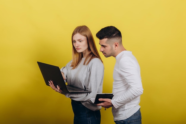 Garota feliz com namorado olhando para laptop em fundo amarelo Eles estudam juntos Resolvem problemas Aprendendo o conceito de trabalho