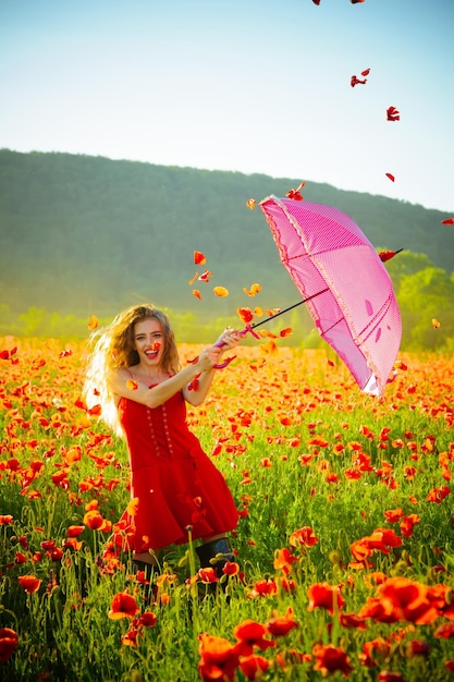 Garota feliz com o guarda-chuva rosa sobre o campo de papoulas vermelhas