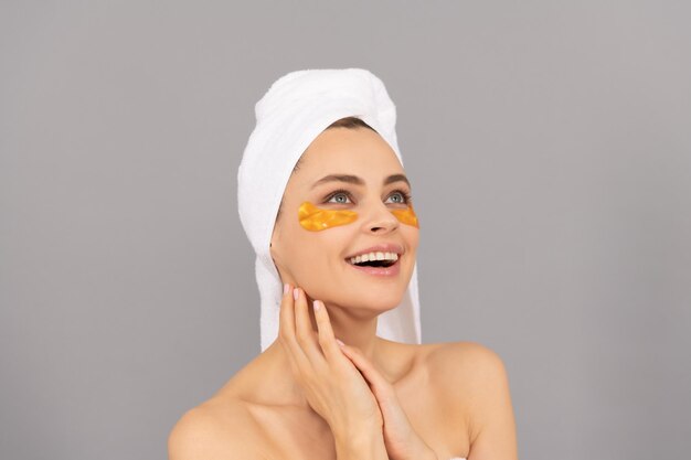 Garota feliz com toalha felpuda usa tapa-olho dourado facial para pele saudável