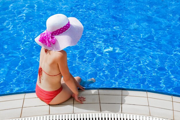 Garota feliz com um chapéu à beira da piscina no mar