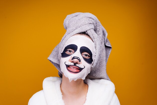 Garota feliz com uma toalha na cabeça sorrindo, na máscara do rosto com o focinho de um panda