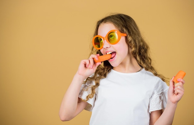 Garota feliz come cenoura fresca férias de verão menina em óculos de moda Vitamina nutrição suco de vitamina refrescante Cuidados de saúde Verão vitamina dieta Fonte natural de vitamina Caloria e dieta