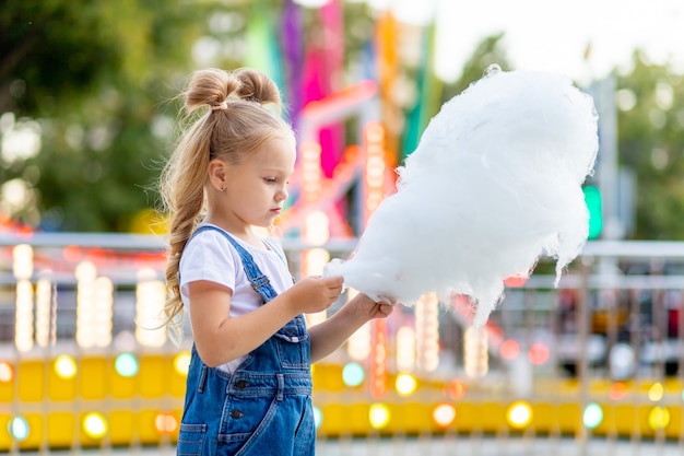 Garota feliz comendo algodão doce no parque de diversões no verão