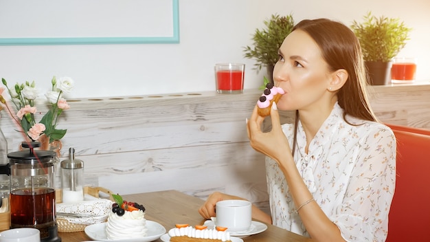 Garota feliz comendo bolo saboroso com frutas em uma loja de doces moderna