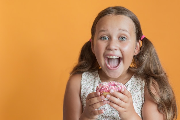 Garota feliz comendo donat na parede laranja