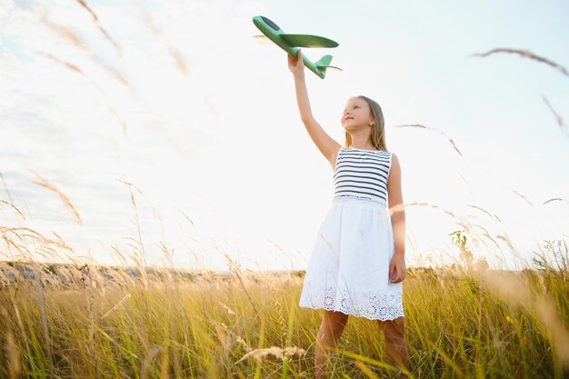 Garota feliz corre com um avião de brinquedo em um campo na luz do sol crianças brincam de avião de brinquedo adolescente sonha em voar e se tornar piloto garota quer se tornar piloto e astronauta câmera lenta