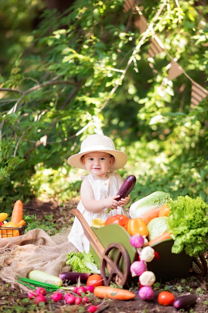 Garota feliz cozinha salada de legumes na natureza. Um pequeno jardineiro recolhe uma colheita de vegetais.