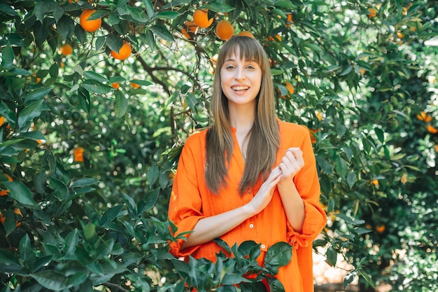 Garota feliz de vestido laranja está olhando para a câmera segurando as mãos juntas no jardim laranja