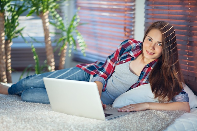 Garota feliz deitada no sofá e trabalhando em um laptop