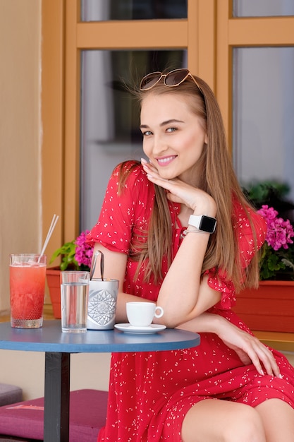 Garota feliz, descansando no terraço do café com um copo de bebida gelada