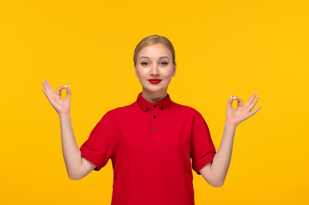 Garota feliz do dia da camisa vermelha mostrando gesto de sinal zen em uma camisa vermelha em um fundo amarelo